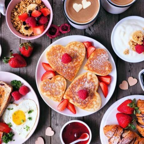 Scène de table de petit-déjeuner pour la Saint-Valentin ou la fête des mères sur un fond de bois sombre avec des crêpes en forme de coeur, des œufs et de la nourriture sur le thème de l'amour