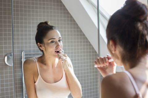 femme d'âge adulte se brosser les dents dans le miroir de salle de bains.