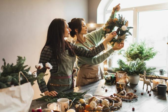 deux femmes fabriquant une couronne de Noël à l'aide de branches de pin fraîches et de décorations festives